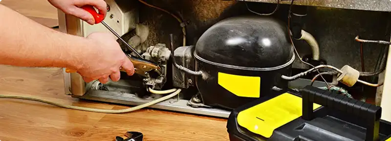 Refrigerator repair technician fixing the compressor and wiring in Garden Grove, CA