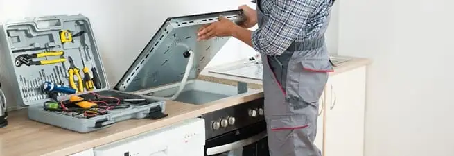 Cooktop repair technician lifting a built-in stovetop for service in Santa Ana, CA