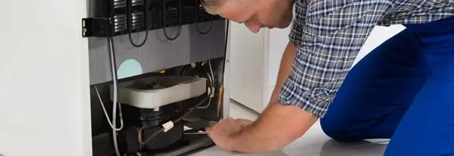 Refrigerator repair technician servicing the compressor and condenser area in Santa Ana, CA