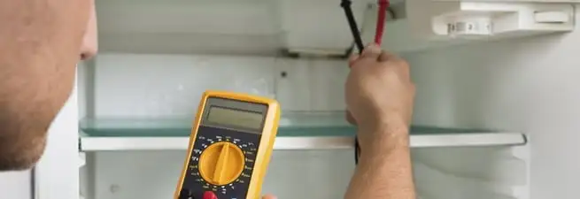 Refrigerator repair technician testing electrical components with a multimeter in Santa Ana, CA